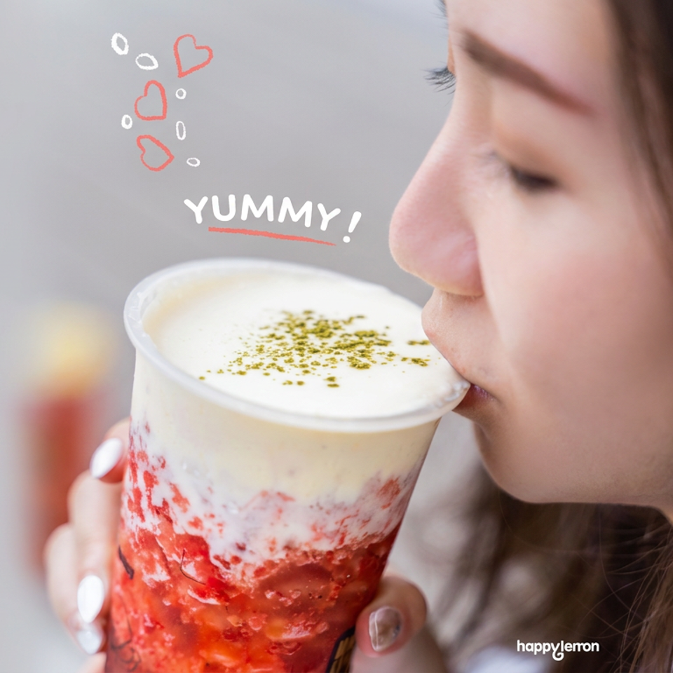 Woman sipping a layered strawberry cream drink topped with green sprinkles, with playful “YUMMY!” lettering above.