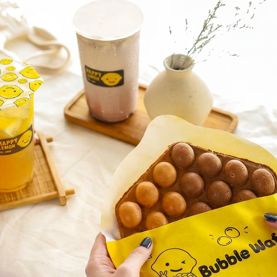 Bubble waffle with chocolate and plain spheres alongside iced lemon tea and milk tea on wooden trays.
