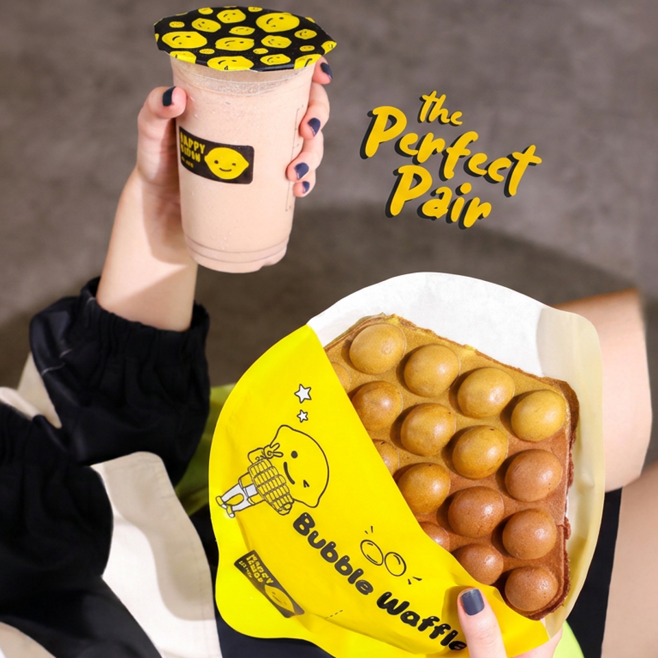 Hands hold a branded smoothie and packaged bubble waffle against a gray background with yellow promotional lettering.