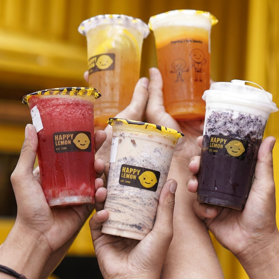 Hands hold five colorful Happy Lemon drinks against a bright yellow background, including red, creamy, purple, and orange beverages.