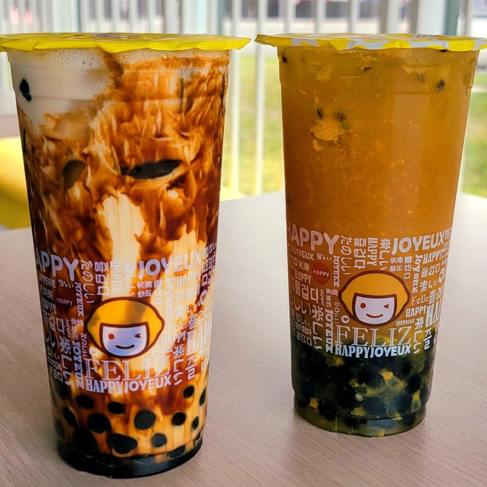 Two branded bubble tea drinks with tapioca pearls sit on a café table, one creamy brown and one amber-colored.